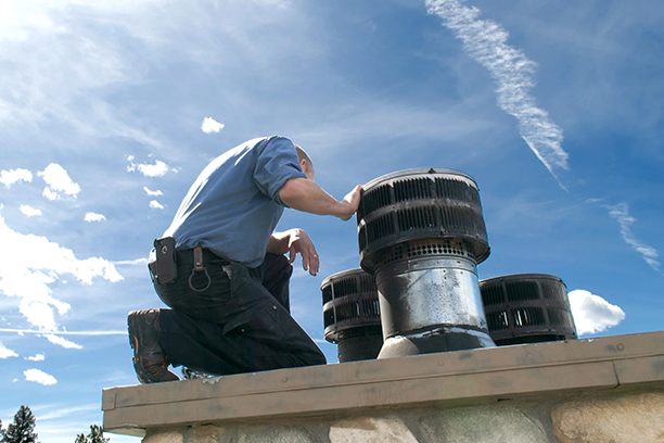 Worker Inspecting Chimney on Rooftop Under Blue Sky